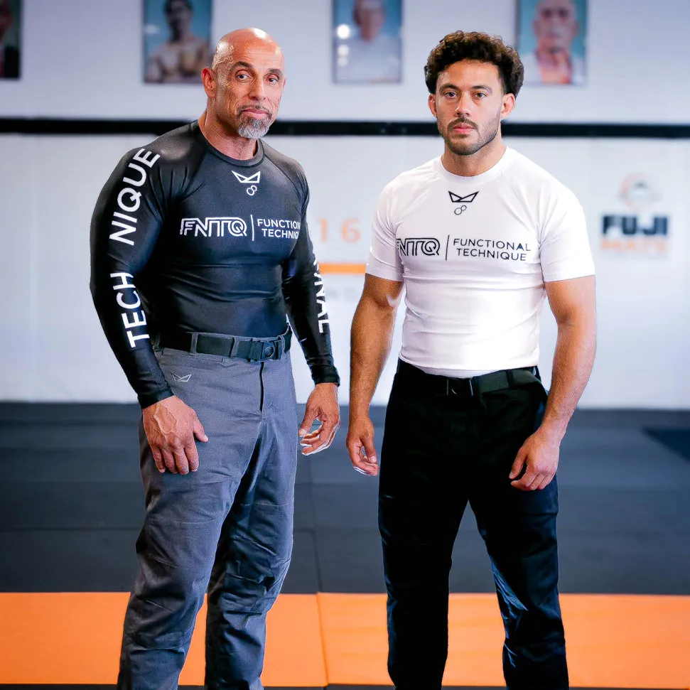 Two athletes in FNTQ rashguards and gi pants stand ready on the mats
