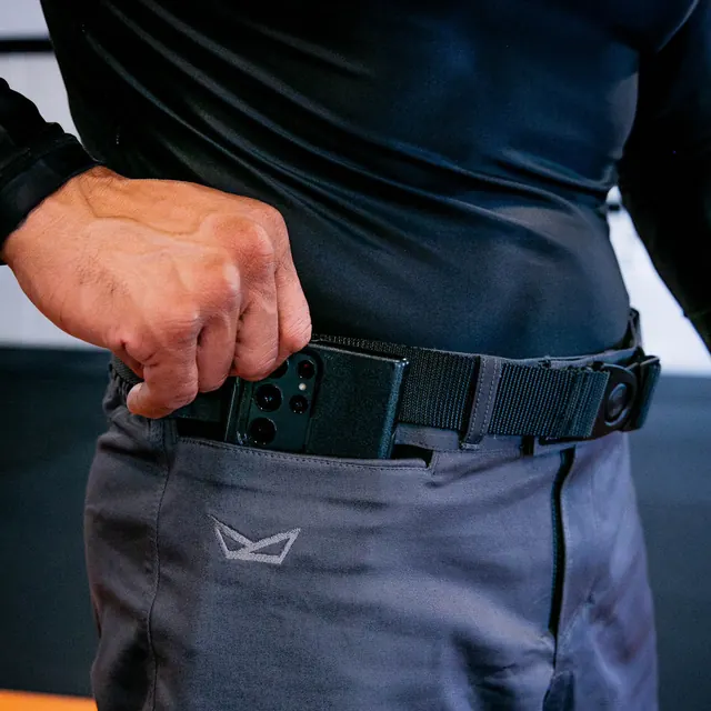 A hand slides a phone into the pocket, belt buckled